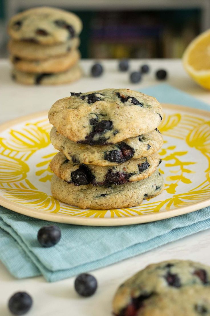 three blueberry cookies on a yellow and white plate with lemons in the background