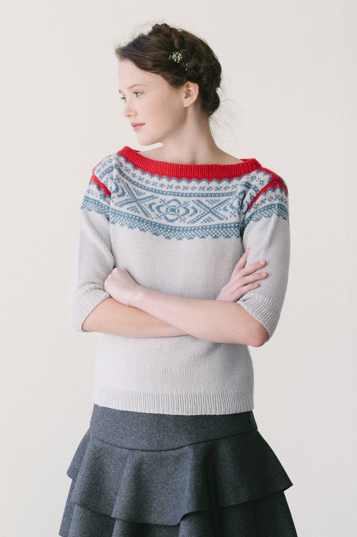 a woman with her arms crossed standing in front of a white wall wearing a sweater and skirt