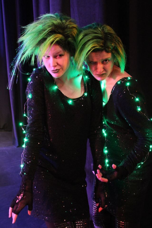 two women dressed in black with green lights on their body and hair are standing next to each other