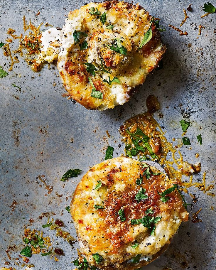 two crab cakes on a baking sheet covered in cheese and herbs, ready to be eaten