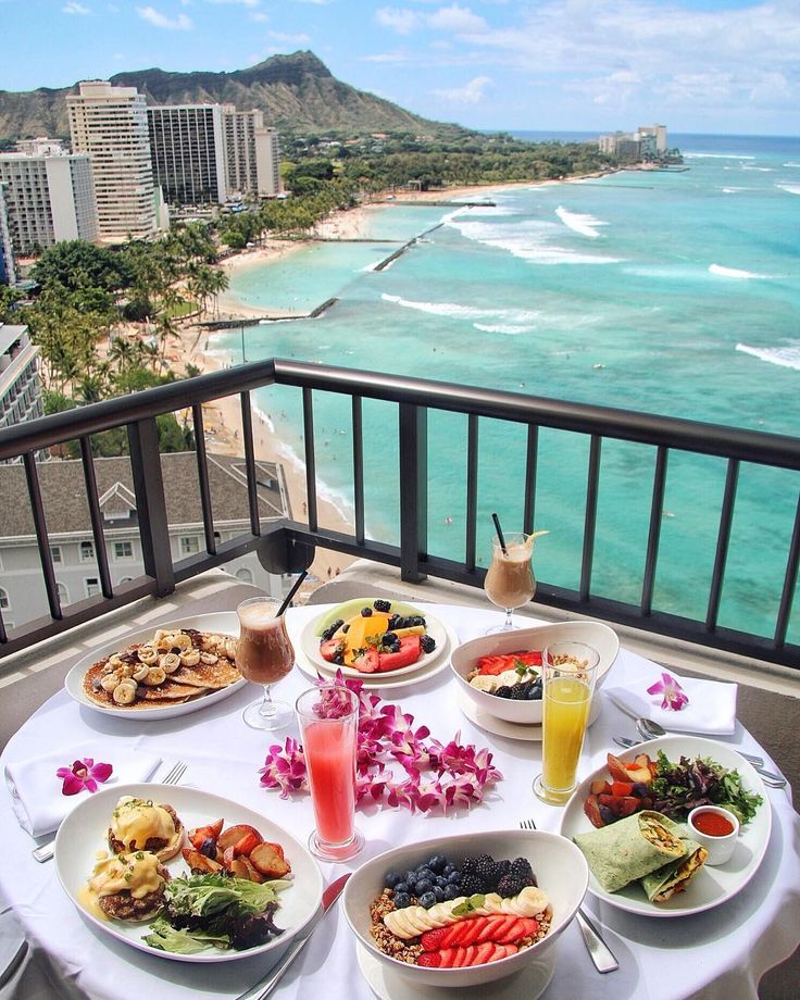 a table topped with plates of food on top of a balcony next to the ocean