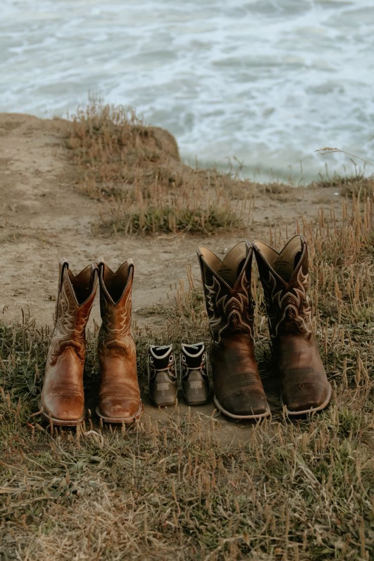 four pairs of cowboy boots are sitting on the grass by the water's edge