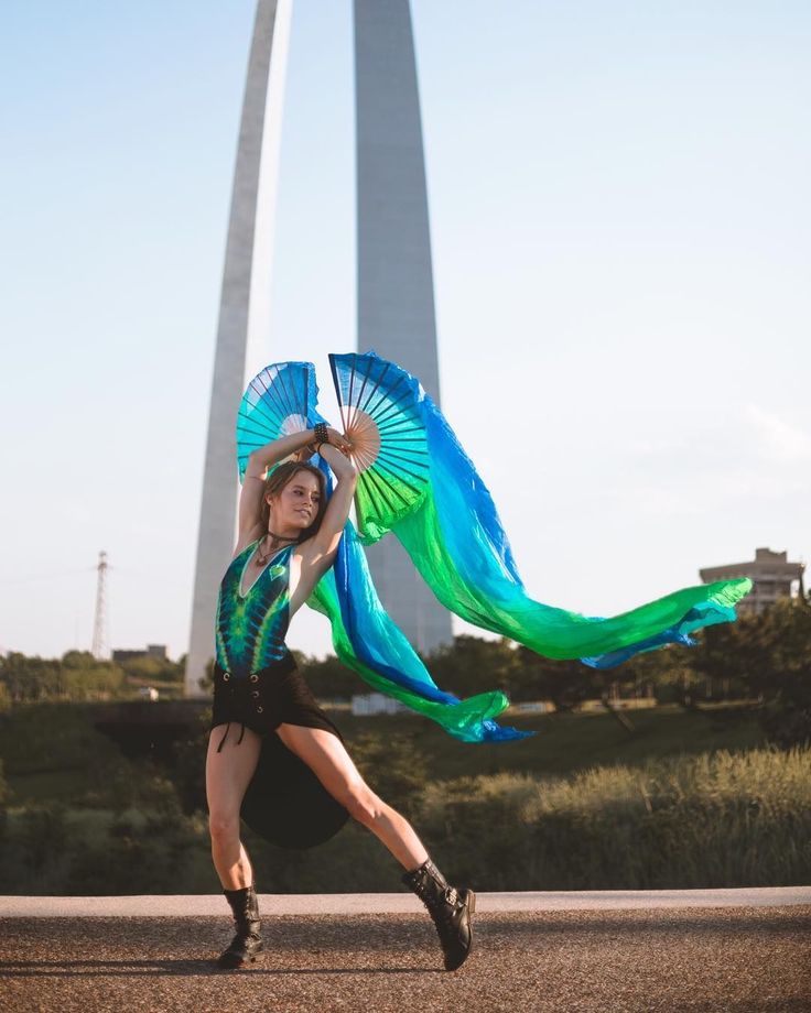 a woman is dancing in front of the st louis arch with her blue and green parasol