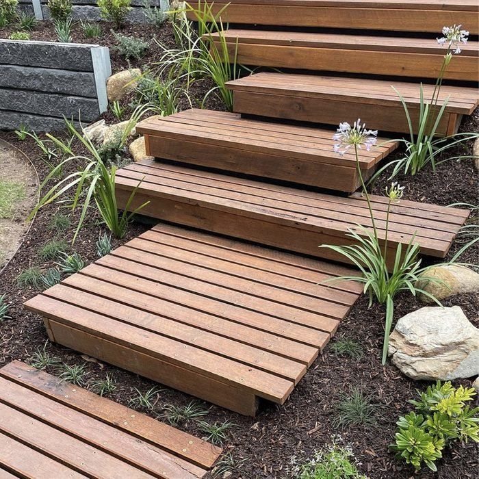 several wooden steps are lined up in the grass near some rocks and flowers on the ground