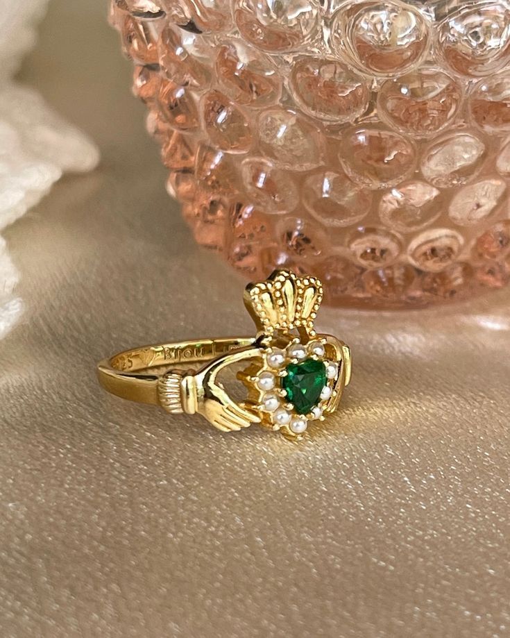 The Irish Promise Ring a traditional Claddagh ring was a design from love. Especially for the Irish lovers! Perfect for a queen and stacks well.This Beautiful ring is 18kt gold plated silver with emerald cubic zirconia and faux pearls. Promise Cubic Zirconia Emerald Birthstone Ring, May Birthstone Hallmarked Diamond Promise Ring, Hallmarked Diamond Promise Ring For May Birthstone, Yellow Gold Jeweled Rings As Gifts, Gold Heart Ring With Center Stone, Yellow Gold Rings With Jewels For Gift, Fine Jewelry Gold Heart Ring With Center Stone, Diamond Promise Ring For May Birthstone, Emerald Birthstone Ring For Promise