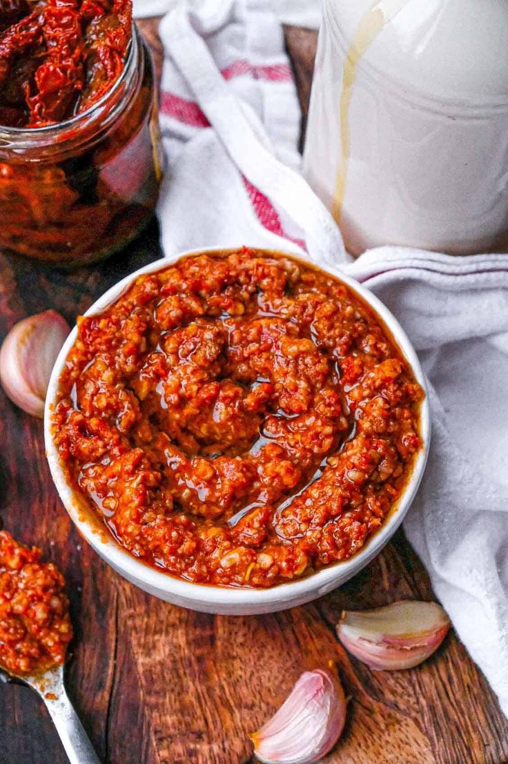 a white bowl filled with chili sauce next to garlic on a cutting board and spoon