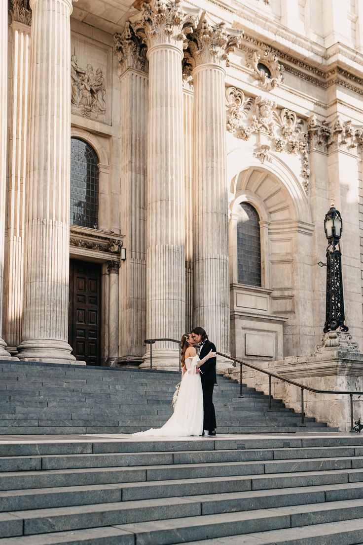 a bride and groom standing on the steps of an old building in front of columns