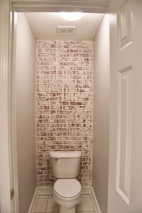 a white toilet sitting inside of a bathroom next to a wall with bricks on it