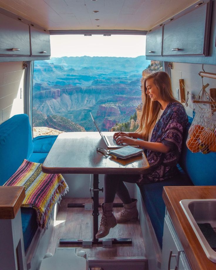 a woman sitting at a table in the back of a camper with a laptop