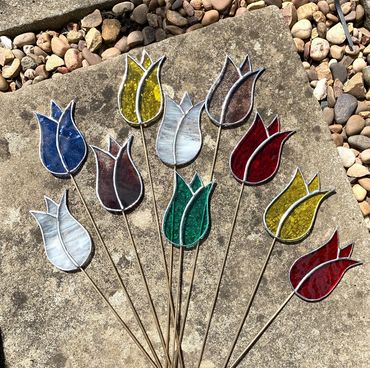 a bunch of colorful glass flowers sitting on top of a stone slab next to some rocks