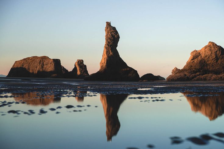 the rocks are reflected in the water on the beach