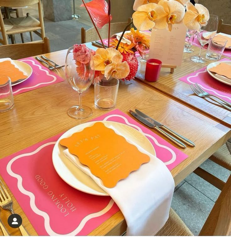 the table is set with pink and orange place mats, napkins, and silverware