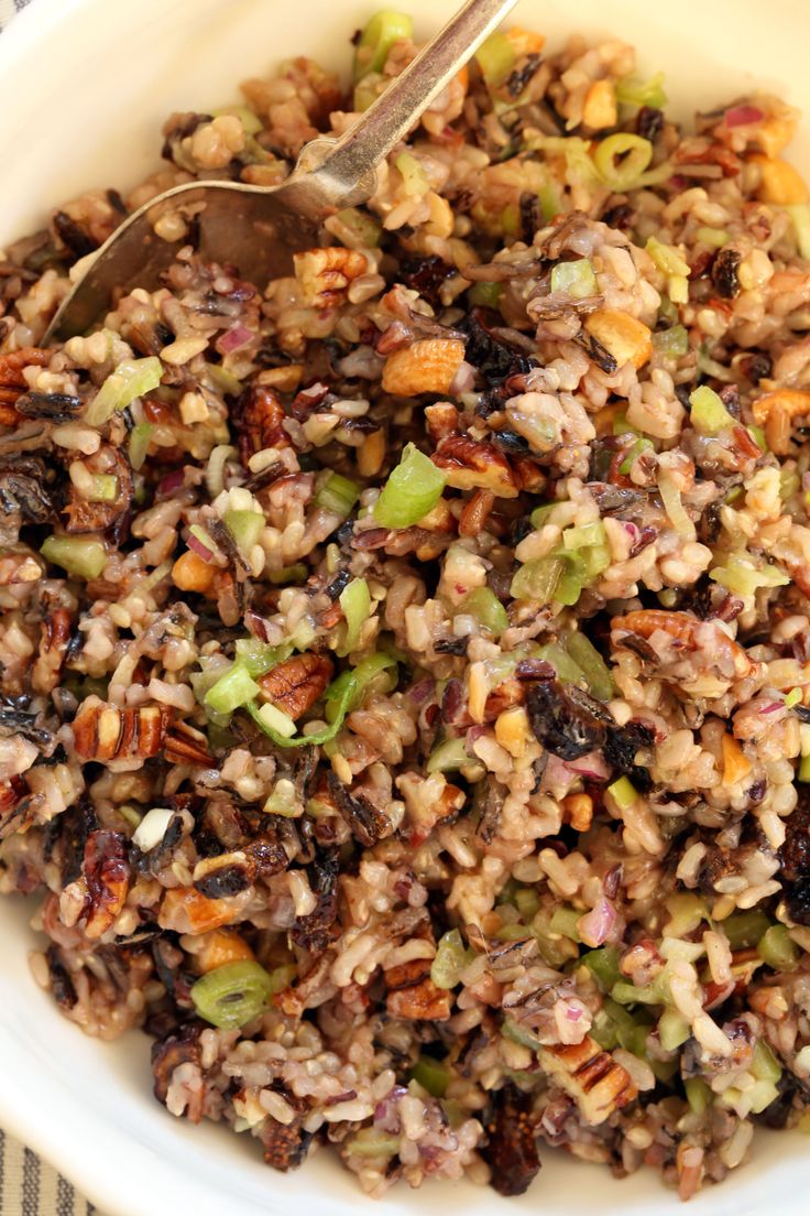 a white bowl filled with brown rice and nuts next to a spoon on a table