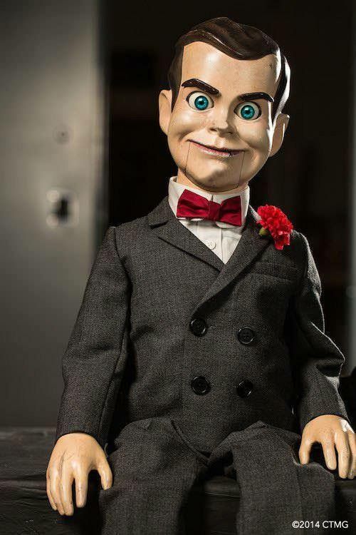 a creepy doll sitting on top of a table wearing a suit and red bow tie