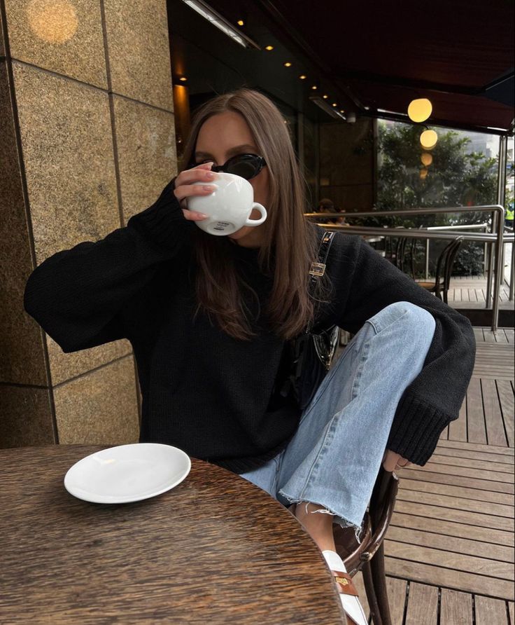 a woman sitting at a table drinking from a cup