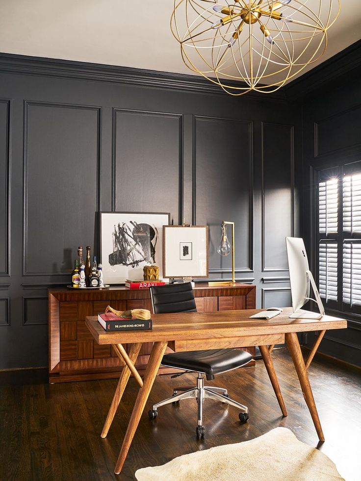 a home office with black walls and wooden flooring, an artful chandelier hangs above the desk