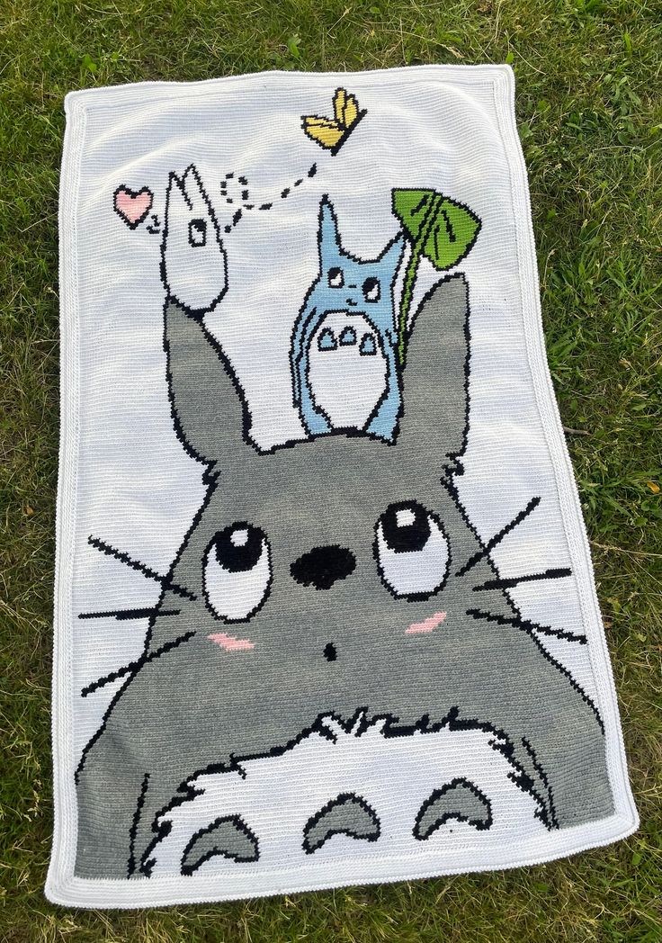 a towel with an image of totoro and cat on it sitting in the grass