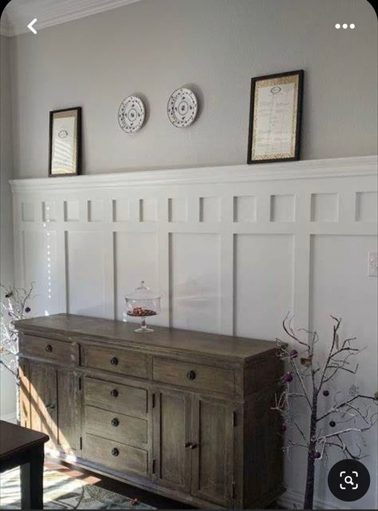 a wooden dresser sitting next to a wall with pictures on it's sideboard