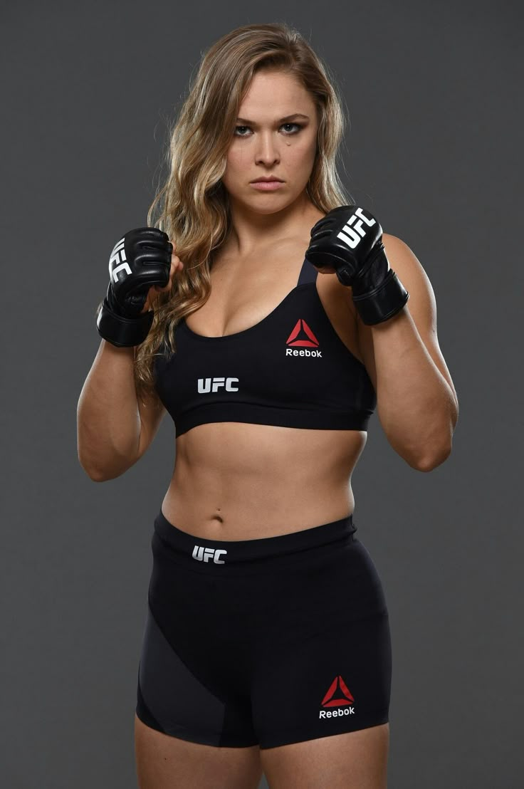 a female fighter posing for the camera with her hands on her hips and wearing boxing gloves