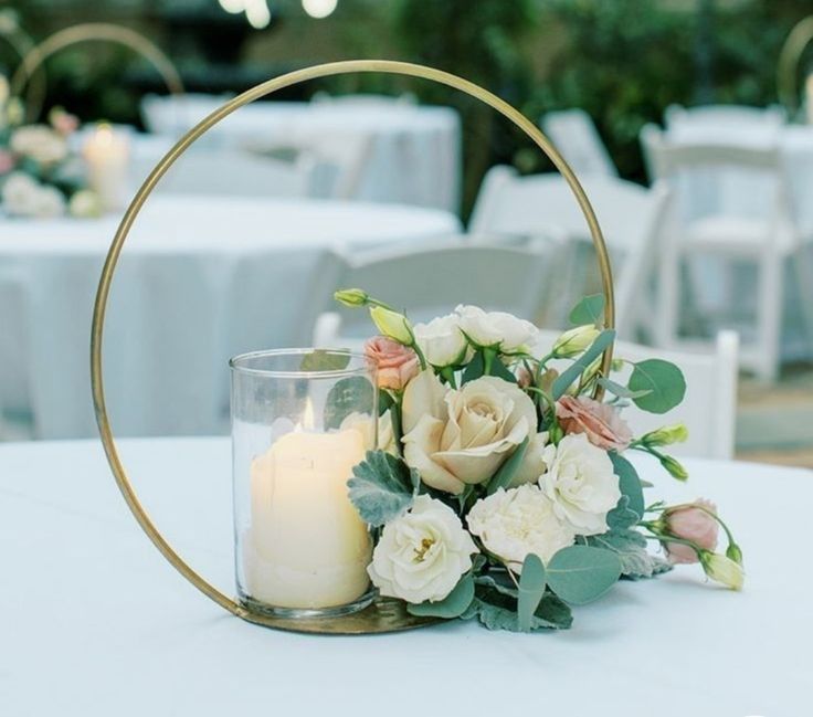 a white table topped with a vase filled with flowers next to a candle and some chairs