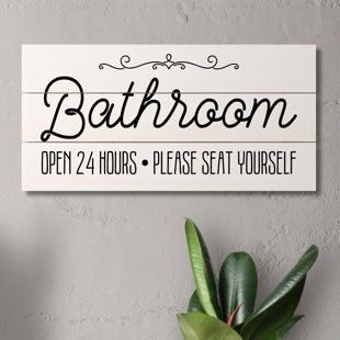 a bathroom sign hanging on the wall next to a potted plant