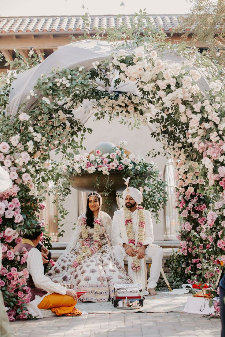 the bride and groom are sitting in front of an archway with pink flowers on it