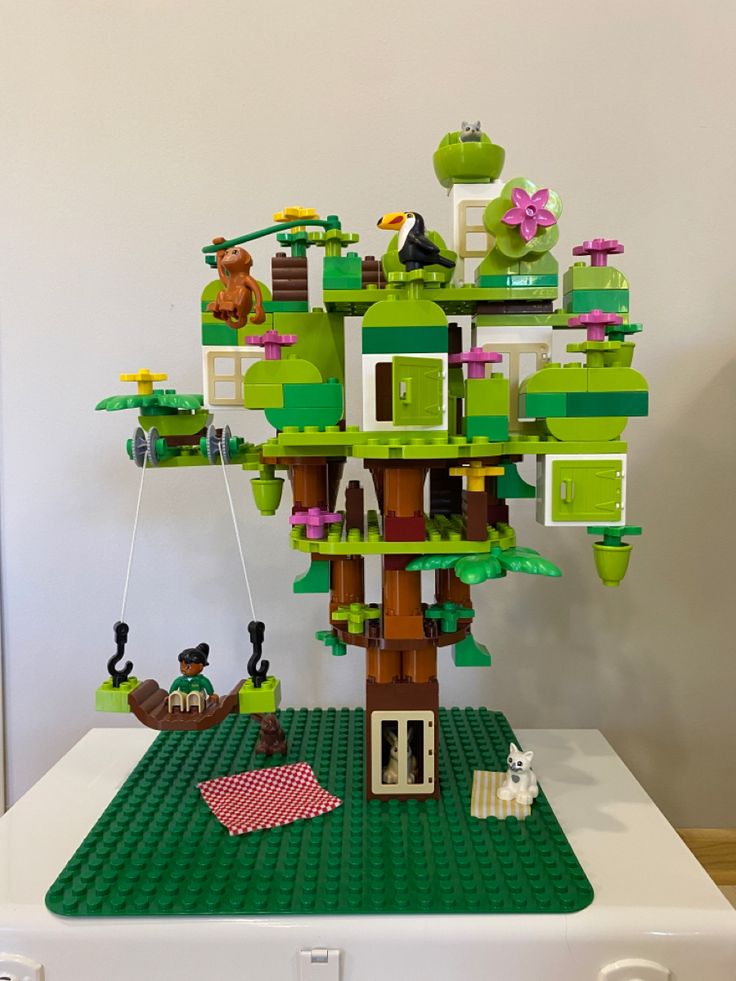 a lego tree with animals and people in it on top of a white table next to a wall