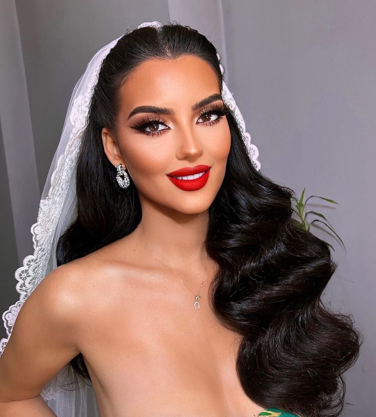 a woman with long hair wearing a wedding veil and red lipstick is posing for the camera