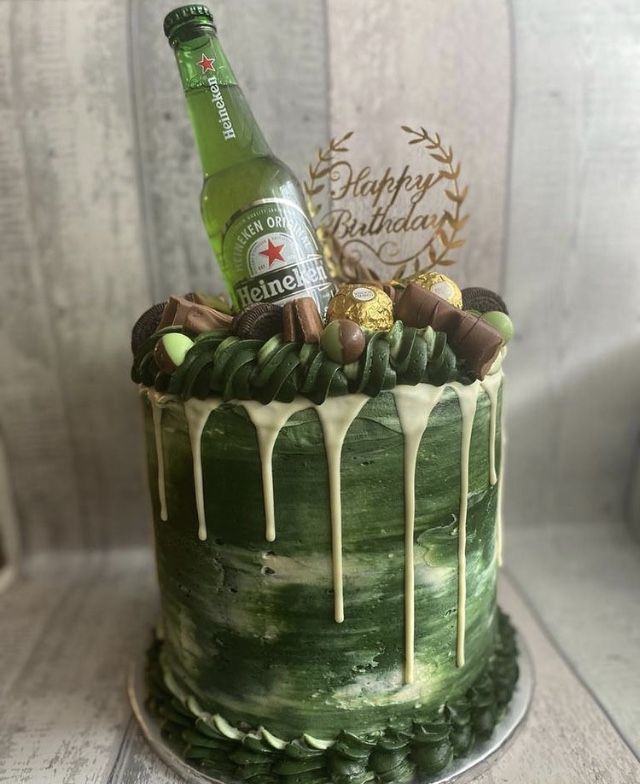 a green cake with white icing and chocolates on top, topped with a bottle of beer