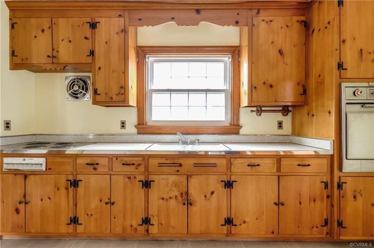 an empty kitchen with wooden cabinets and white stove top oven in the center, next to a window