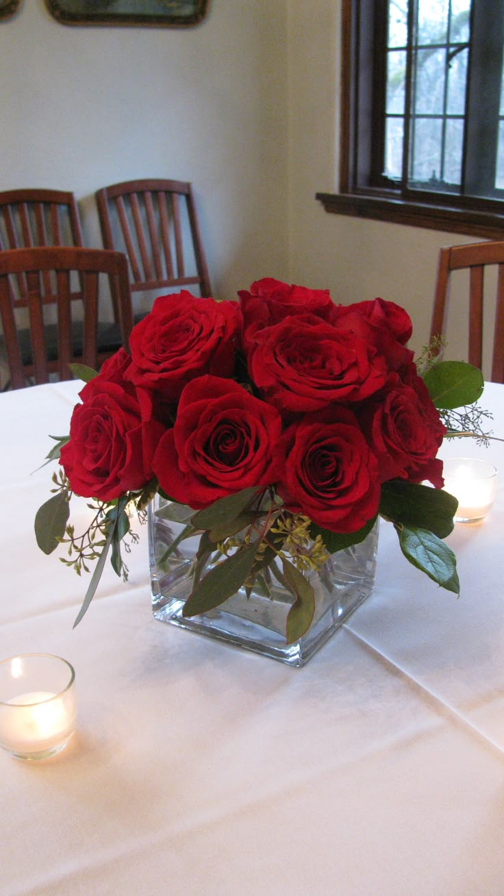 a vase filled with red roses sitting on top of a white tablecloth covered table