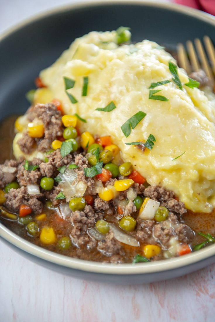 a bowl filled with mashed potatoes, meat and veggies next to a fork