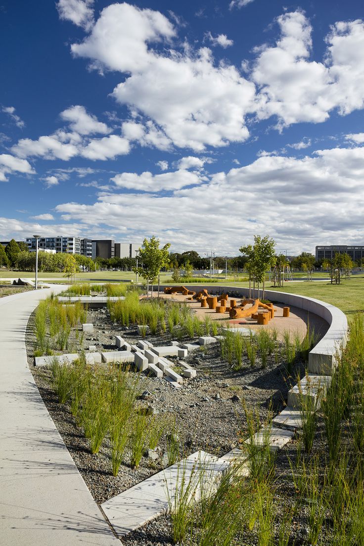 an empty park with benches and plants in the foreground under a blue sky with white clouds