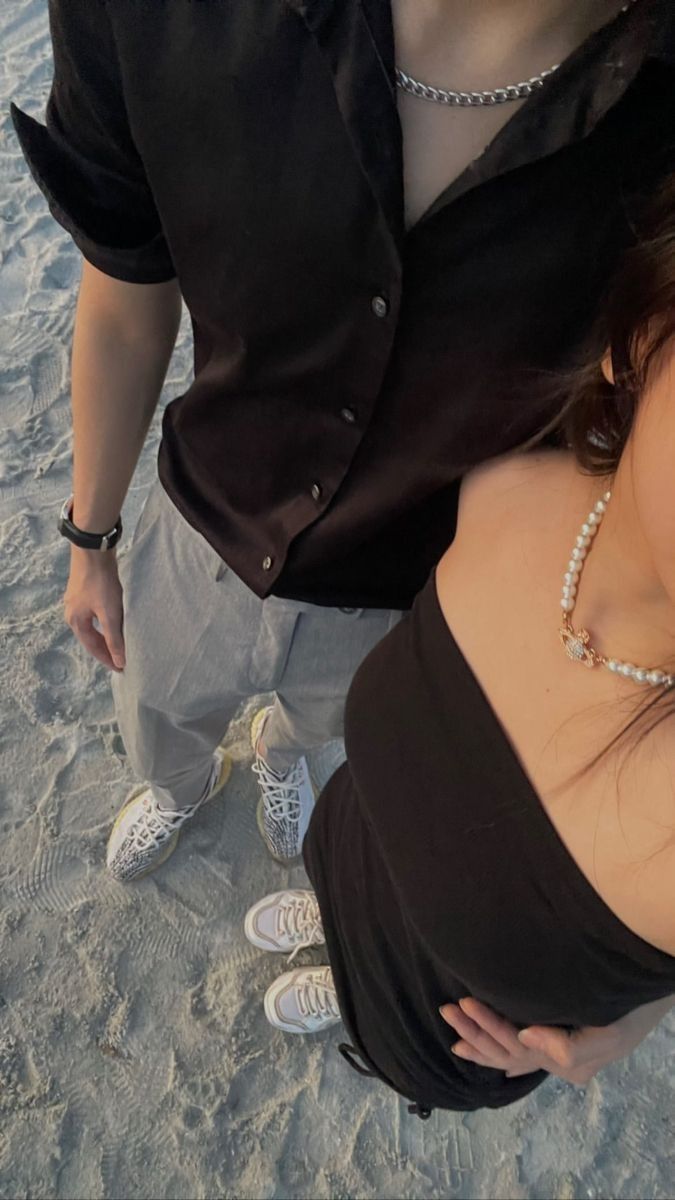 a man and woman standing next to each other on the beach with their hands behind their backs