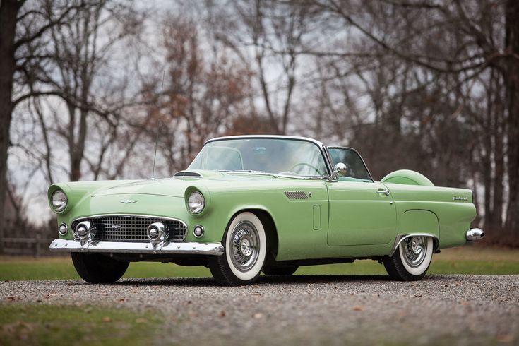 an old green car parked on the side of a road in front of some trees