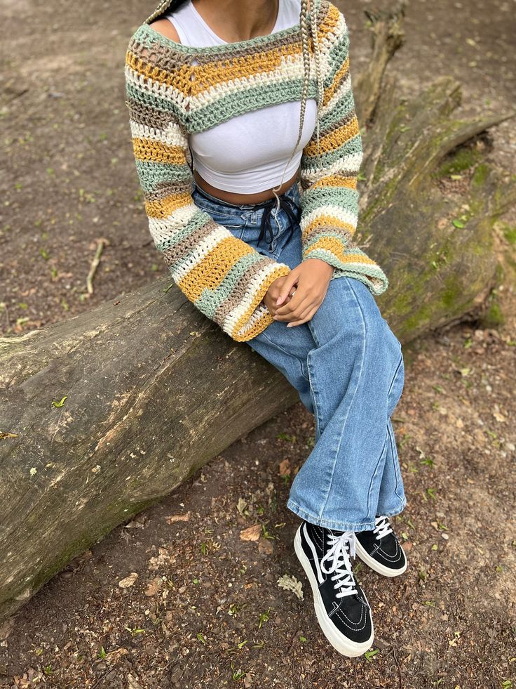 a woman sitting on top of a tree branch wearing a colorful knitted sweater and jeans