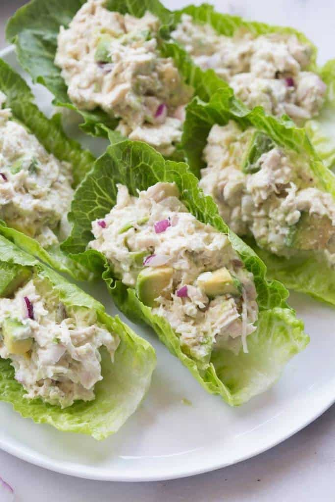 several lettuce leaves with chicken salad on them sitting on a white plate, ready to be eaten