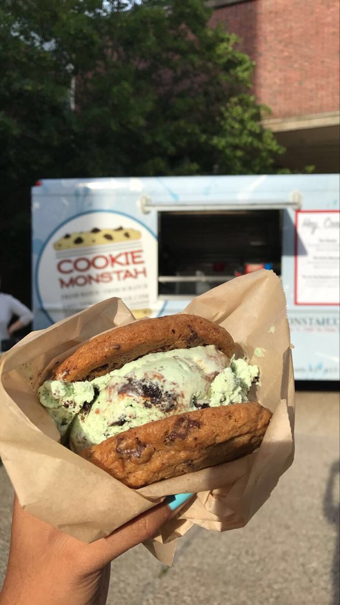 a person holding up a sandwich with ice cream on it in front of a food truck