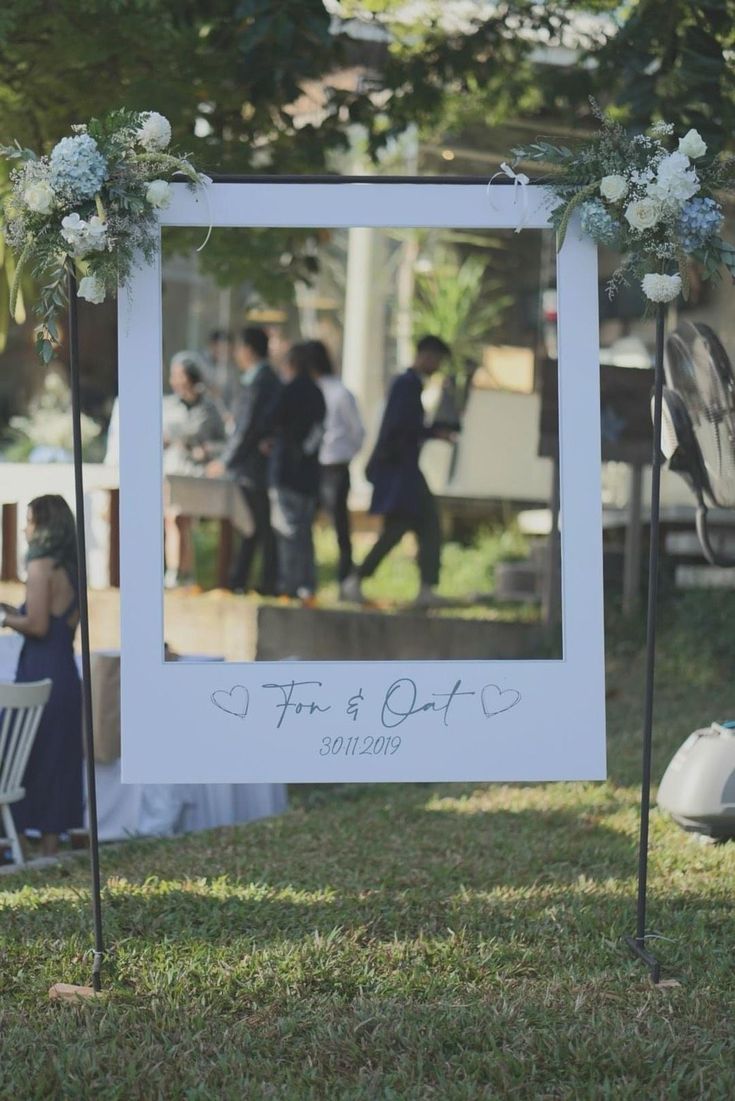 a photo frame with flowers on it sitting in the grass next to some chairs and tables