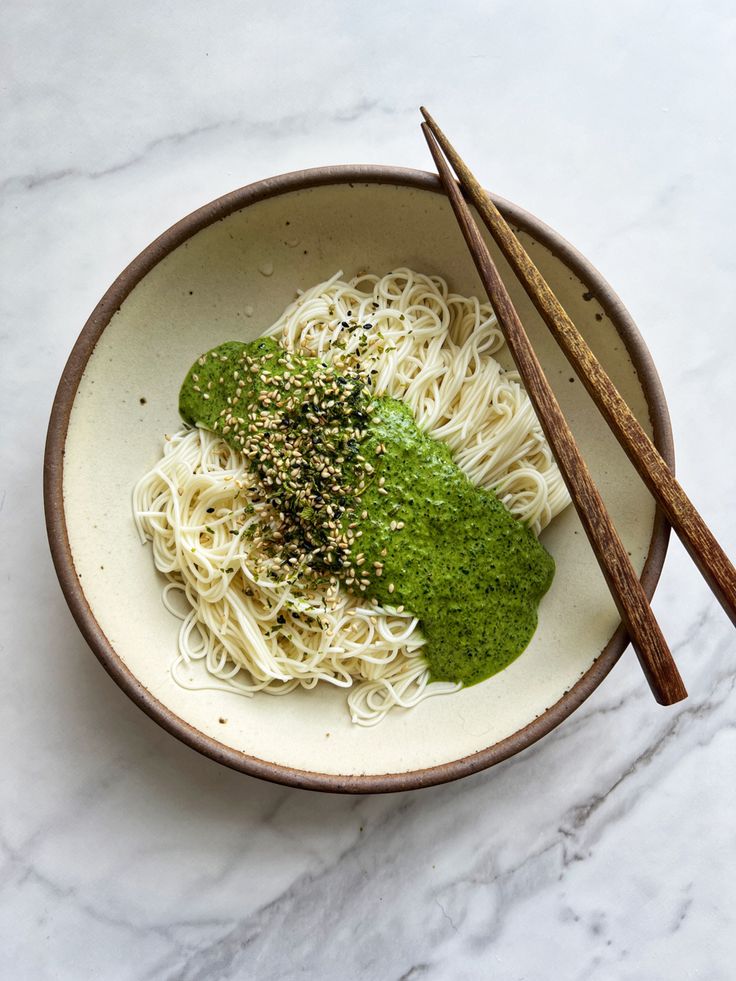 a white bowl filled with noodles and sauce next to chopsticks on a marble surface