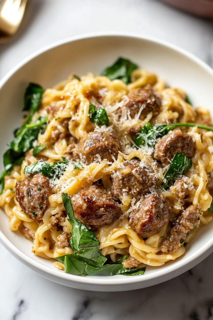 a white bowl filled with pasta and meat on top of a marble table next to silverware