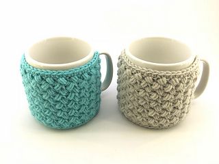 two crocheted coffee mugs sitting next to each other on a white surface