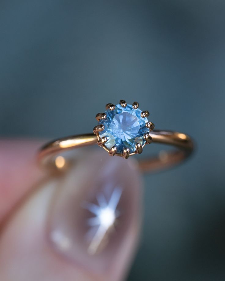 a close up of a person's hand holding a ring with a blue stone