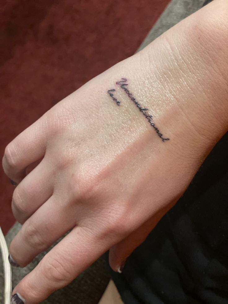 a person with a small tattoo on their left hand and the word love written in cursive writing