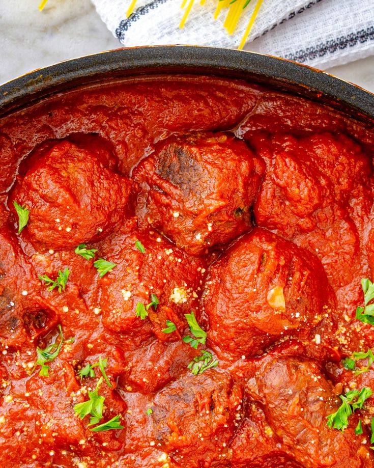 a pan filled with meatballs covered in marinara sauce and garnished with parsley