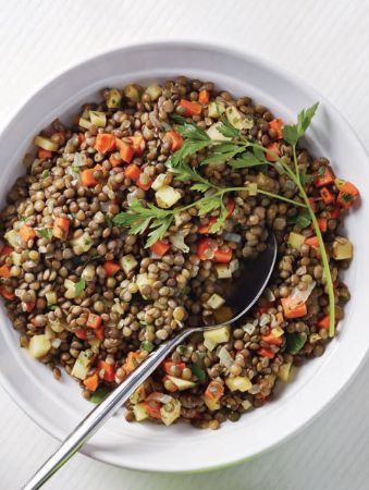 a bowl filled with lentils and carrots on top of a white table next to a spoon