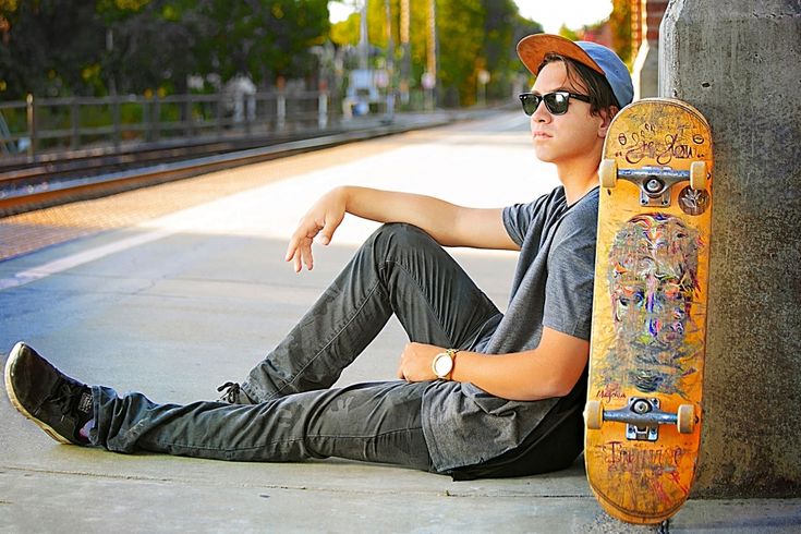 a young man sitting on the ground with his skateboard in front of him,