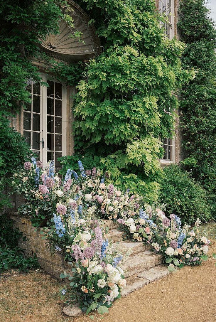 an old house with flowers and ivy growing on the outside wall, along with stone steps leading up to it's front door