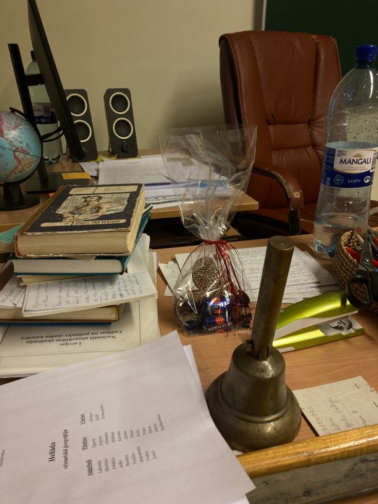 a wooden desk topped with lots of books and papers next to a bottle of water