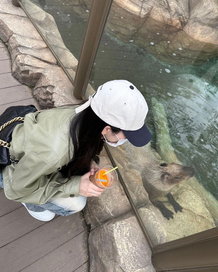 a woman holding an orange in her hand while looking at a bear through a glass window